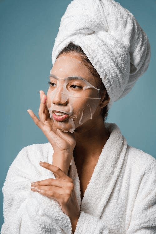Free Smiling young ethnic female applying sheet mask on face after shower Stock Photo